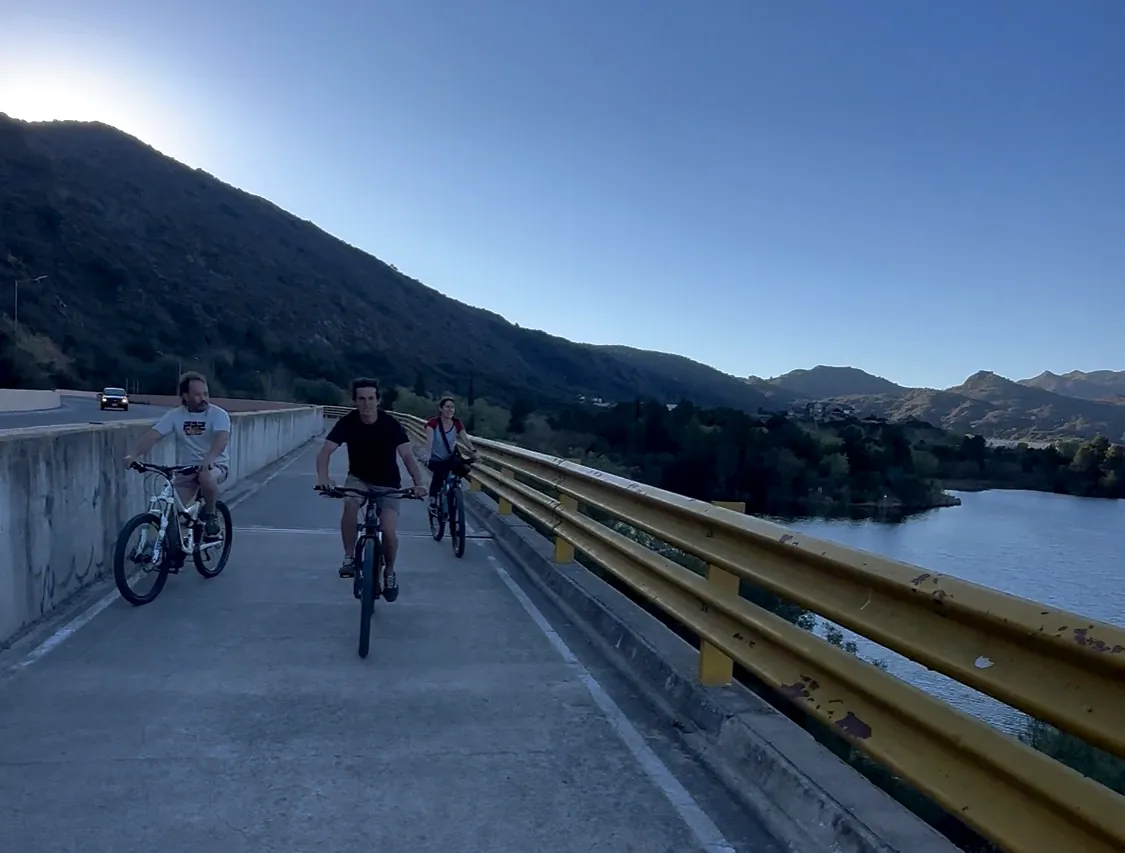 Grupo de ciclistas pedaleando por el paredón del dique de Potrero de los Funes al atardecer